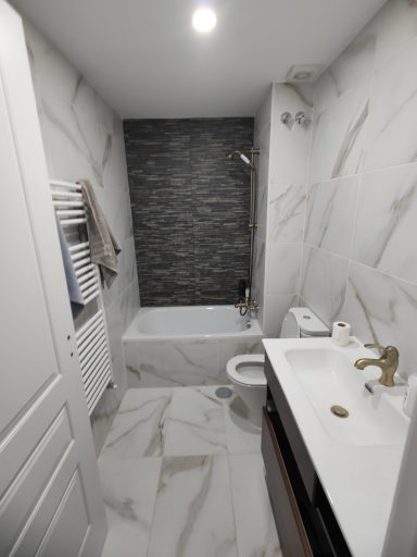 Baño moderno con ducha, bañera y azulejos de mármol. Lavabo con grifo dorado.
