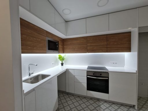 Cocina moderna con muebles blancos, armarios de madera y luces LED.