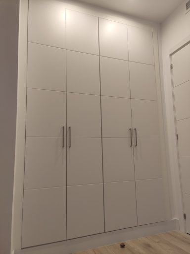 Armario blanco de dos puertas con tiradores plateados en una pared.