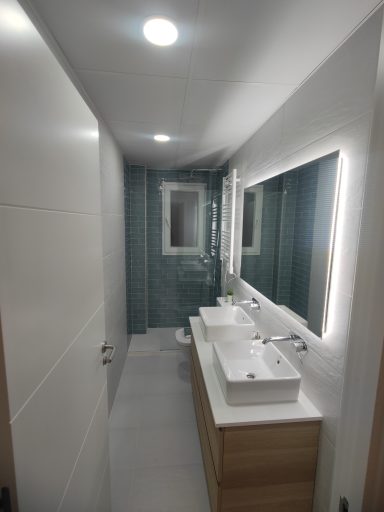 Baño moderno con luz LED, dos lavabos y ducha separada. Paredes en tonos claros.