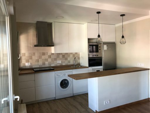 Cocina moderna con electrodomésticos integrados y barra de madera.