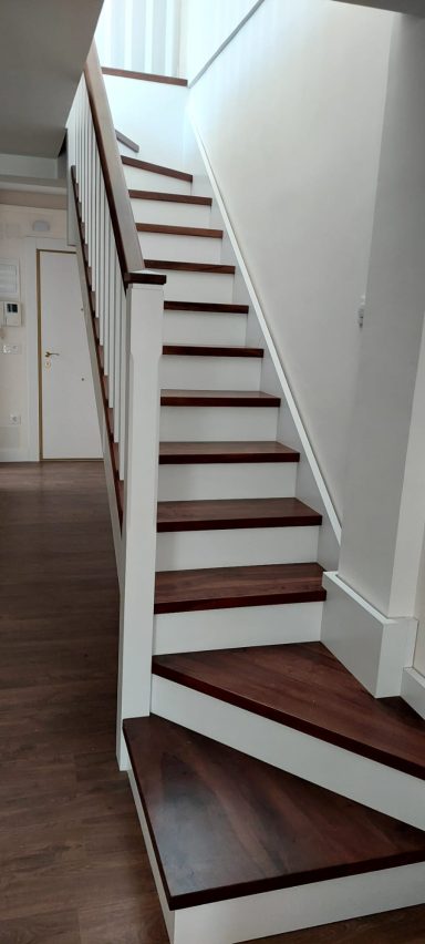 Escalera moderna de madera con barandilla blanca en un pasillo iluminado.