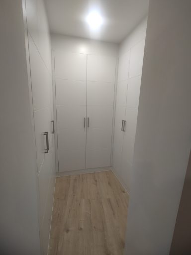 Pasillo con puertas de armario blancas y suelo de madera clara. Iluminación suave.
